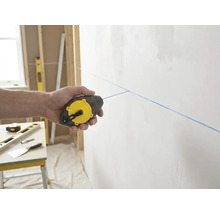 Hand nutzt ein Stanley Schlagschnurgerät für eine blaue Markierungslinie an einer Wand in einer hellen und organisierten Baustellenszenerie.
