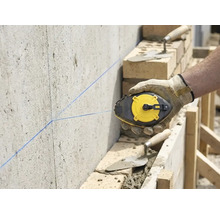Handwerker markiert mit einem Schlagschnurgerät eine gerade Linie an einer Betonwand auf einer Baustelle mit Mauerwerk.