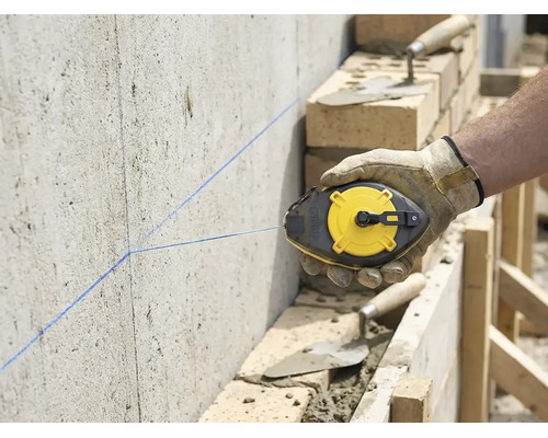 Handwerker markiert mit einem Schlagschnurgerät eine gerade Linie an einer Betonwand auf einer Baustelle mit Mauerwerk.