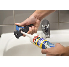 Hände schneiden die Düse einer Soudal Sanitärsilikon-Kartusche mit einem Fugenschneider über einem Waschbecken im Badezimmer ab.