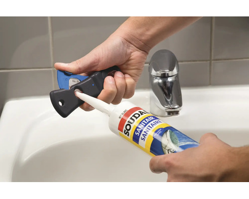 Hände schneiden die Düse einer Soudal Sanitärsilikon-Kartusche mit einem Fugenschneider über einem Waschbecken im Badezimmer ab.