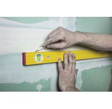 Eine Wasserwaage wird an eine Wand gehalten, während eine Person mit einem Bleistift eine Markierung entlang der Oberkante zeichnet.
