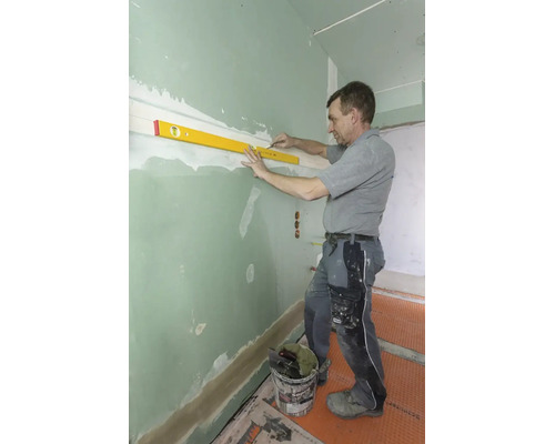 Handwerker nutzt eine Wasserwaage und einen Bleistift, um eine waagerechte Linie an einer grünen Trockenbauwand zu markieren.