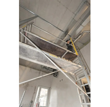 Handwerker auf einem Layher Fahrgerüst bei der Installation an einer Betondecke im Rohbau.