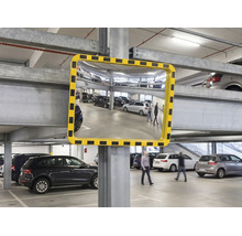 Konvexer Sicherheitsspiegel mit gelb-schwarz gestreiftem Rahmen in einer hellen Parkgarage zur Verbesserung der Sichtbarkeit.
