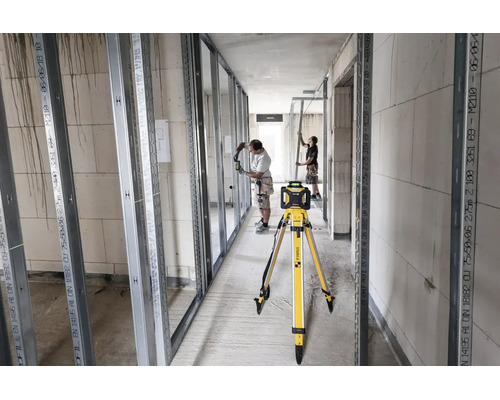Stabila Rotationslaser auf Stativ auf einer Baustelle für den Innenausbau mit Metallprofilen und zwei Handwerkern.