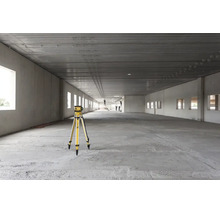 Rotationslaser auf einem Stativ in einem großen, hellen Industrierohbau mit Betonboden und hohen Decken.