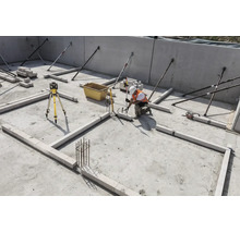Bauarbeiter auf einer Baustelle nutzt einen Rotationslaser und eine Messlatte zum Ausrichten von Mauersteinen auf dem Betonfundament.