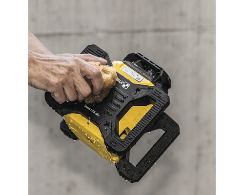 Eine Hand reinigt den wasserfesten Stabila Rotationslaser LAR 160 mit einem Schwamm vor einer Betonwand.