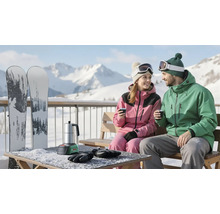 Paar in Wintersportbekleidung sitzt auf einer Holzbank auf einem verschneiten Balkon vor Bergen. Auf dem Tisch steht ein Bosch Akku-Espressokocher.