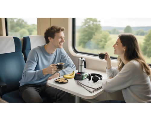 Zwei Personen im hellen Zugabteil an einem Tisch mit mobilem Bosch Espressokocher, Tassen, Keksen, Bananen, Kopfhörern und einer Zeitung.