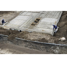 Baustelle mit einer Betonplatte, Bewehrungsstahl und Bauarbeitern bei der Erstellung eines Fundaments.