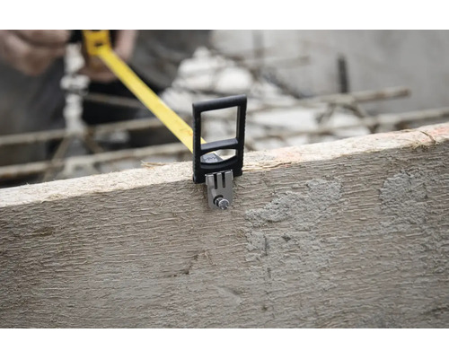 Gelbes Rollmaßband an einem Holzbalken auf einer Baustelle angesetzt.
