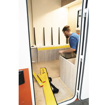 Ein Mann installiert Holzkomponenten mit einer Stabila Wasserwaage in einem hellen Raum mit hellen Holzpaneelen und weißer Wand.