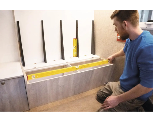 Ein Handwerker nutzt eine Wasserwaage zum präzisen Ausrichten eines hölzernen Möbelstücks.