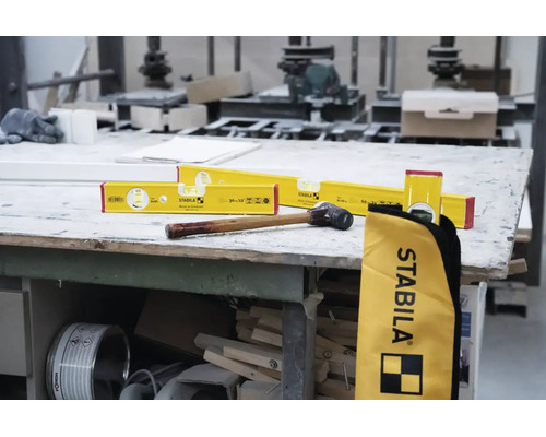 Stabila Wasserwaagen in verschiedenen Größen, ein Hammer mit Holzstiel und eine Stabila Werkzeugtasche auf einer Werkbank in einer Werkstatt.