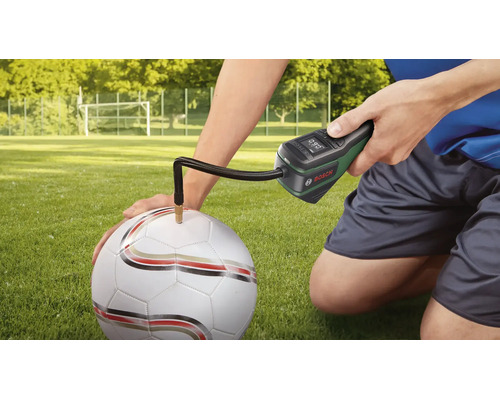 Bosch Akku-Druckluftpumpe beim Aufpumpen eines Fußballs auf einem Rasenplatz.