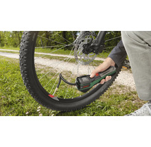 Hand hält eine Bosch Akku-Druckluftpumpe und befüllt einen Fahrradreifen im Freien.