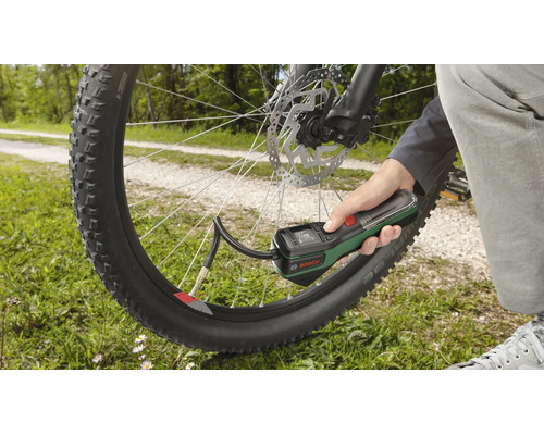 Hand hält eine Bosch Akku-Druckluftpumpe und befüllt einen Fahrradreifen im Freien.