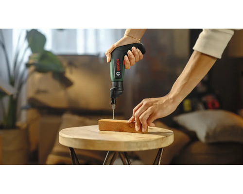Bosch Akku-Schrauber IXO beim Bohren in ein Holzstück auf einem runden Holztisch.