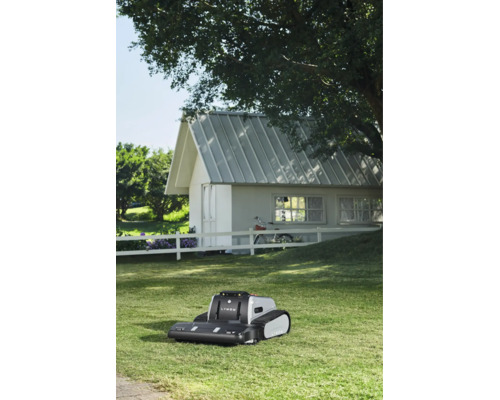 Lymow Mähroboter mit Raupenantrieb auf einem Rasen vor einem weißen Gartenhaus mit weißem Zaun.