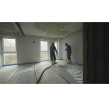 Handwerker verlegen flüssigen Estrich über einer Fußbodenheizung in einem hellen Raum während einer Hausrenovierung.