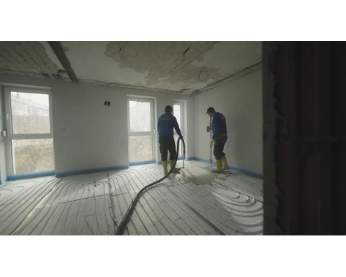 Handwerker verlegen flüssigen Estrich über einer Fußbodenheizung in einem hellen Raum während einer Hausrenovierung.