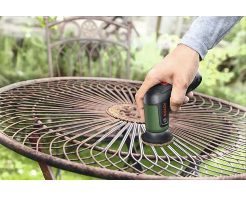 Eine Person benutzt eine Bosch Reinigungsbürste, um Rost von einem runden Metall-Gartentisch zu entfernen.