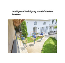 Helle Außenaufnahme einer Sicherheitskamera, die die intelligente Verfolgung einer Person mit Paket auf einem Gehweg vor einem weißen Haus zeigt.