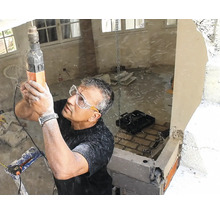 Handwerker mit Schutzbrille bohrt mit einem Bohrhammer in eine Betondecke auf einer Baustelle während einer Hausrenovierung.