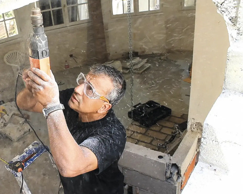 Handwerker mit Schutzbrille bohrt mit einem Bohrhammer in eine Betondecke auf einer Baustelle während einer Hausrenovierung.