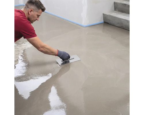 Ein Handwerker verteilt Ausgleichsmasse mit einer Glättkelle gleichmäßig auf einem Boden.