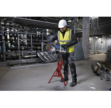 Handwerker schneidet Metallrohr mit Bosch Akku-Bandsäge auf einem roten Rohrständer in einer Industriehalle.