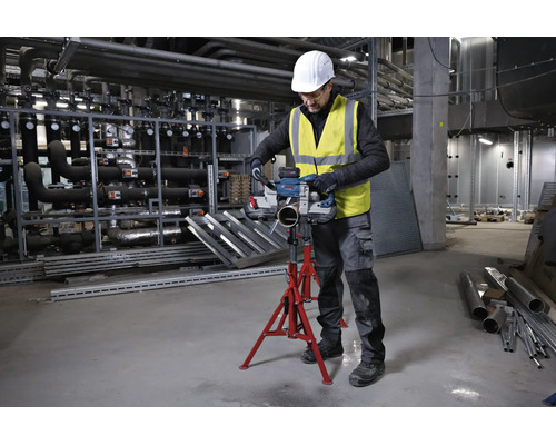 Handwerker schneidet Metallrohr mit Bosch Akku-Bandsäge auf einem roten Rohrständer in einer Industriehalle.