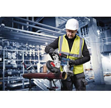 Handwerker nutzt eine Bosch Akku-Bandsäge zum Schneiden eines Metallrohrs in einer Industriehalle.