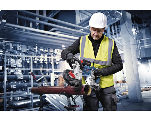 Handwerker nutzt eine Bosch Akku-Bandsäge zum Schneiden eines Metallrohrs in einer Industriehalle.