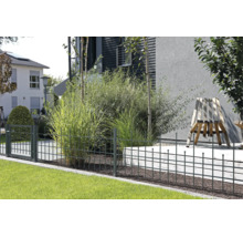 Moderner Metallzaun mit Gartentor in einem gepflegten Garten mit Ziergräsern, Rasenfläche und einem modernen Holzstuhl.