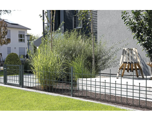 Moderner Metallzaun mit Gartentor in einem gepflegten Garten mit Ziergräsern, Rasenfläche und einem modernen Holzstuhl.