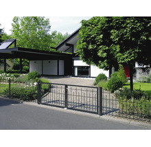 Schwarzer Metallzaun mit zweiflügeligem Tor vor einem modernen Garten und Haus mit gepflasterter Einfahrt.