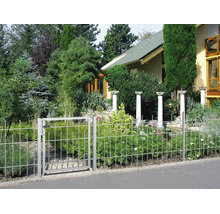Metallzaun mit Gartentor in einem bepflanzten Garten mit Büschen, Bäumen und dekorativen Steinsäulen im Hintergrund.