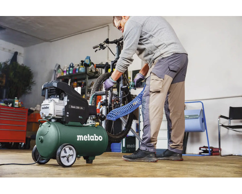 Ein Mann benutzt einen Metabo Basic 200-24 Kompressor in einer hellen Werkstatt, um einen Fahrradreifen aufzupumpen.