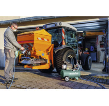 Ein Mann benutzt einen Metabo Kompressor und eine Spritzpistole an einem Streugerät, das an einem Traktor befestigt ist.