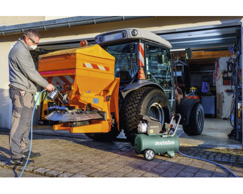 Ein Mann benutzt einen Metabo Kompressor und eine Spritzpistole an einem Streugerät, das an einem Traktor befestigt ist.