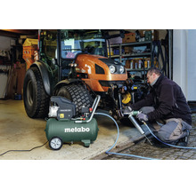 Eine Person nutzt eine Fettpresse an einem Metabo Kompressor Basic 250-50 zur Wartung eines Traktors in einer hellen Werkstatt.