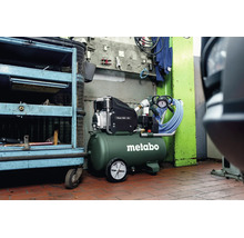 Metabo Kompressor Basic 300-50 in einer Werkstatt mit grünem Druckluftbehälter, schwarzem Motor, Rädern und blauem Druckluftschlauch.