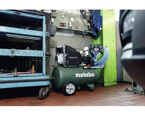 Metabo Kompressor Basic 300-50 in einer Werkstatt mit grünem Druckluftbehälter, schwarzem Motor, Rädern und blauem Druckluftschlauch.