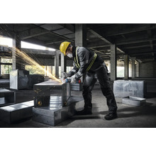 Handwerker in grauer Arbeitskleidung mit Winkelschleifer auf einer Baustelle bei der Bearbeitung von Metallkanälen.