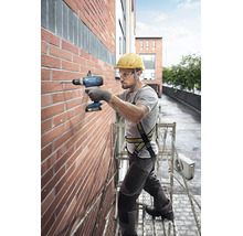 Handwerker bohrt mit Bosch Akku-Schlagbohrschrauber auf einem Gerüst in eine Ziegelwand. Er trägt Helm, Schutzbrille und Sicherheitsgurt.