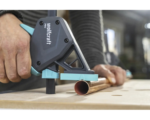 Wolfcraft Einhandzwinge Pro fixiert ein Kupferrohr auf einer hölzernen Werkbank bei der Metallbearbeitung.