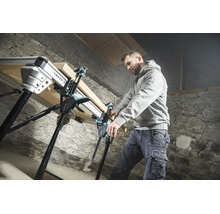 Handwerker fixiert ein Holzbrett mit Einhandzwingen auf einer multifunktionalen Werkbank in einer Werkstatt mit Steinwand.